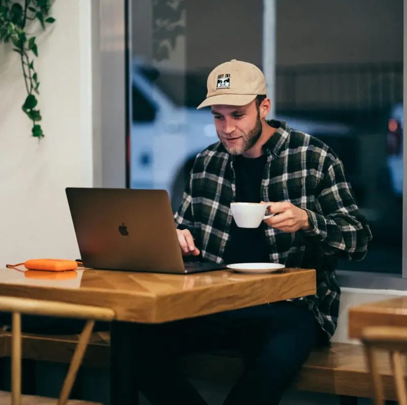 Persona trabajando en su laptop con un cafecito en la mano.