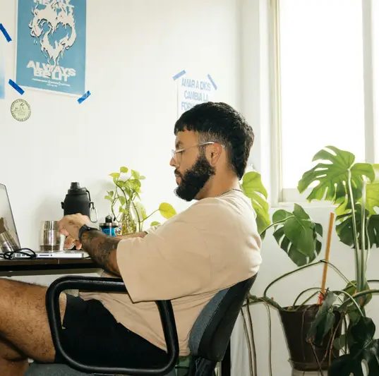 Persona trabajando en su escritorio en casa, rodeada de plantas.